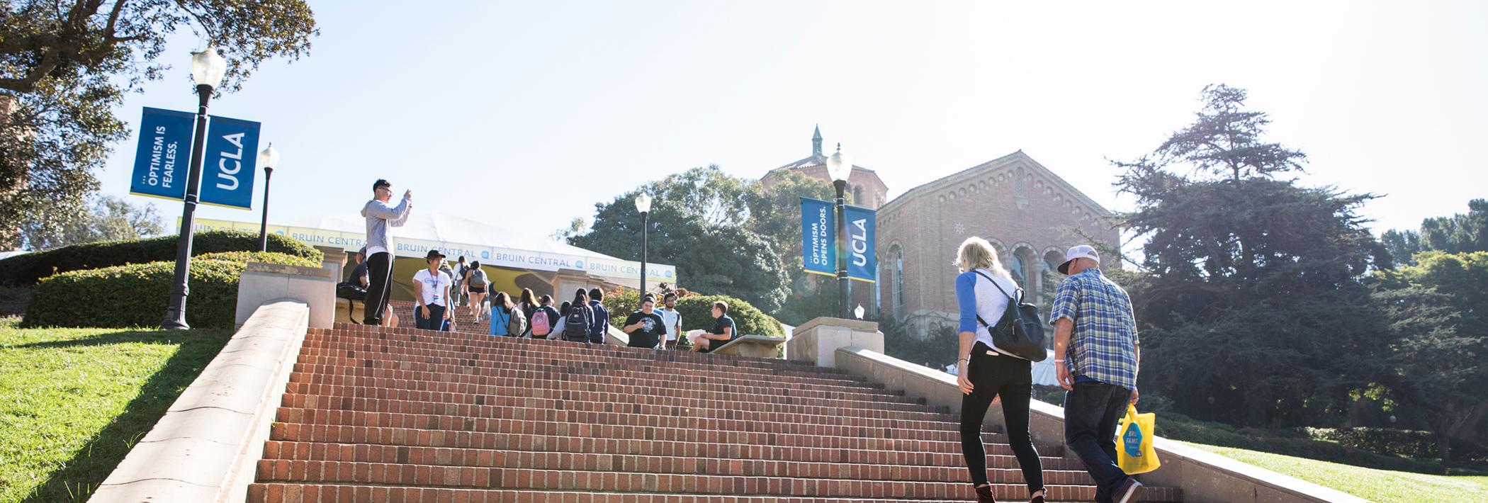 Students climb the Janss steps on a sunny day, Powell library in the distance.